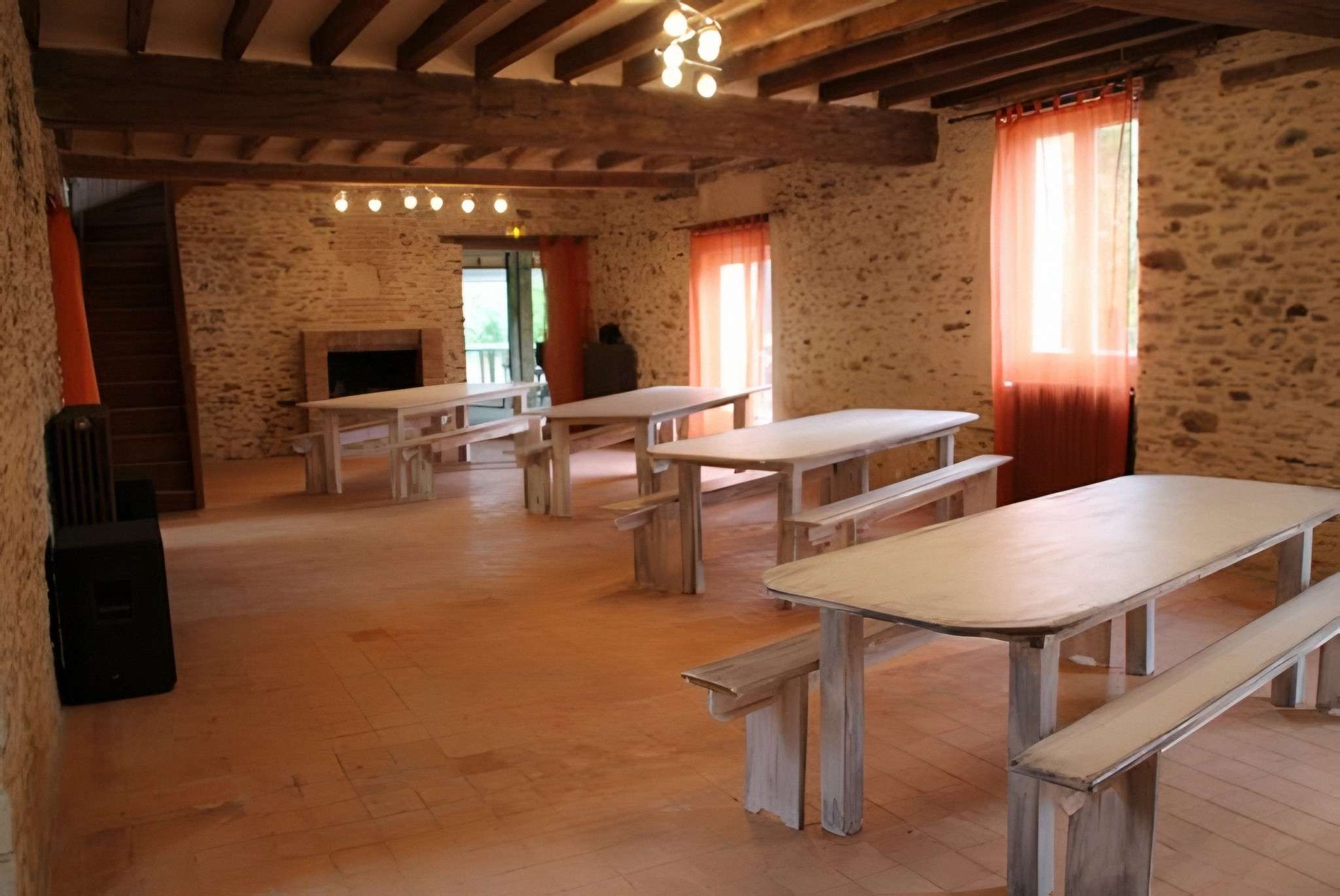 Une salle de La Bâtisse : murs de pierre, cheminée et grandes tables en bois