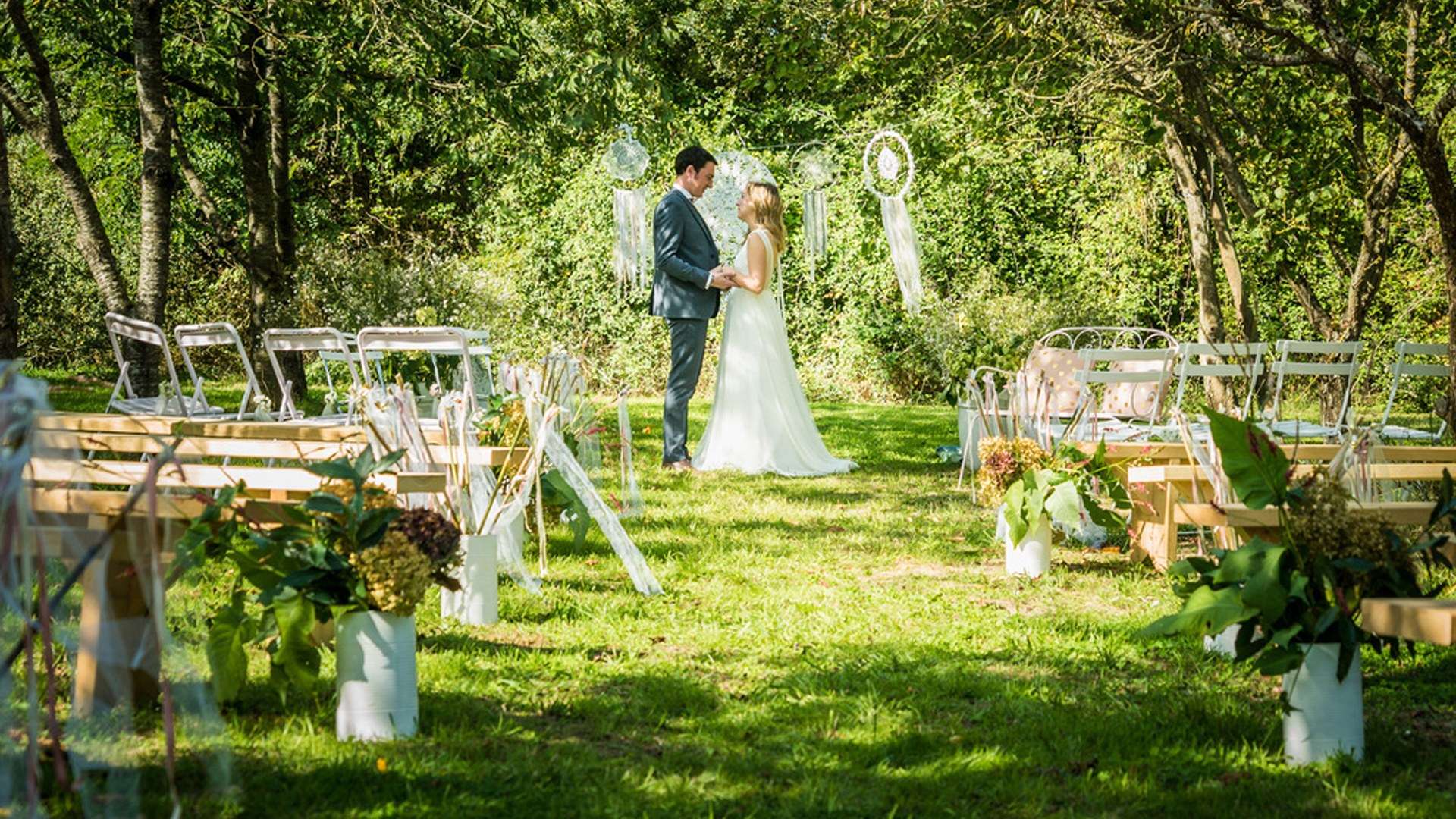 Des mariés sous les pommiers du verger, entre les bancs et les bouquets de la cérémonie