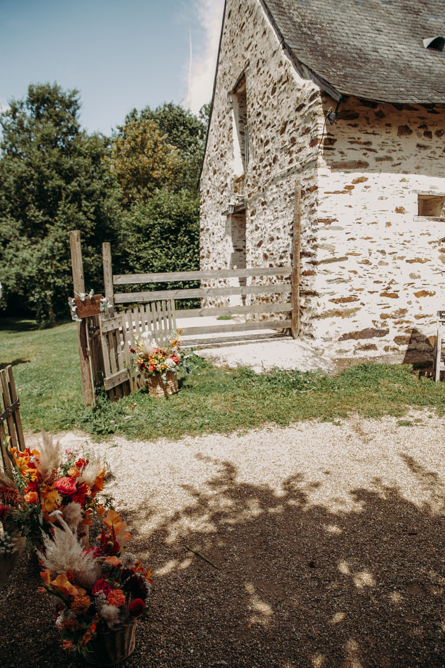 L'entrée du domaine avec un vieux portail en bras le long d'un vieux bâtiment en pierre garni de fleurs dans des pots en osier.