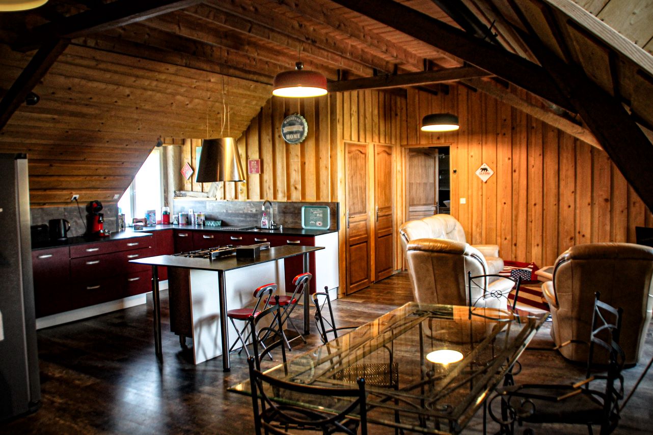 Image de la cuisine équipée et du salon d'un gîte tout en bois, champêtre et conviviale.